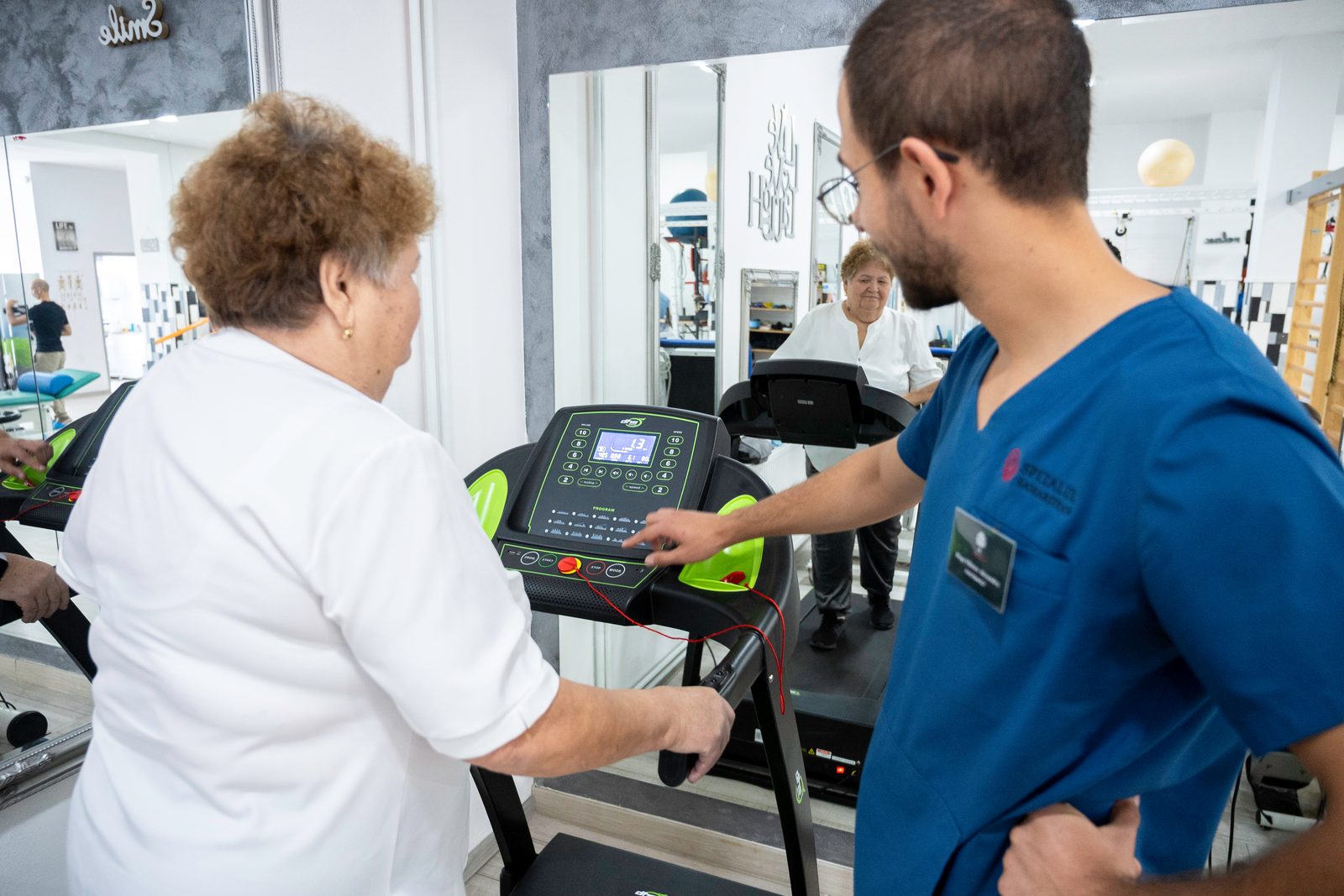 Pacientă pe banda de mers, susținută de kinetoterapeut