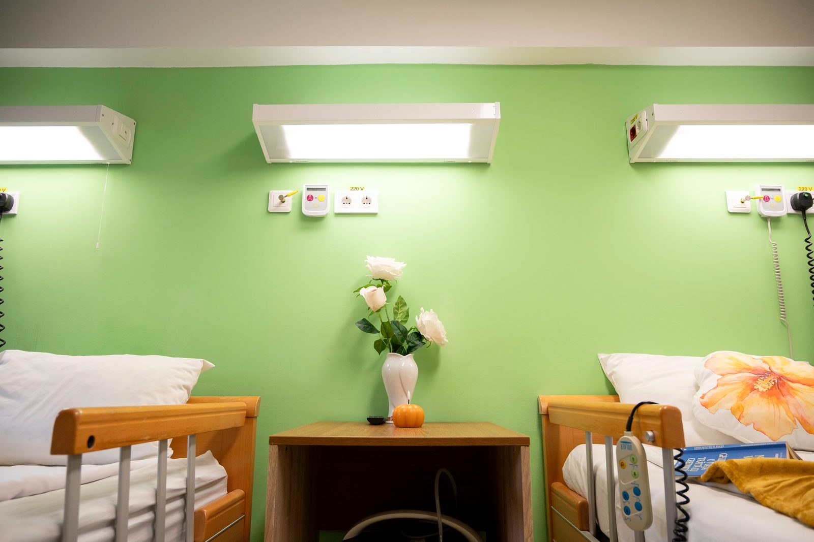 Salon luminos cu paturi medicale, noptieră și flori, la Spitalul Samaritean