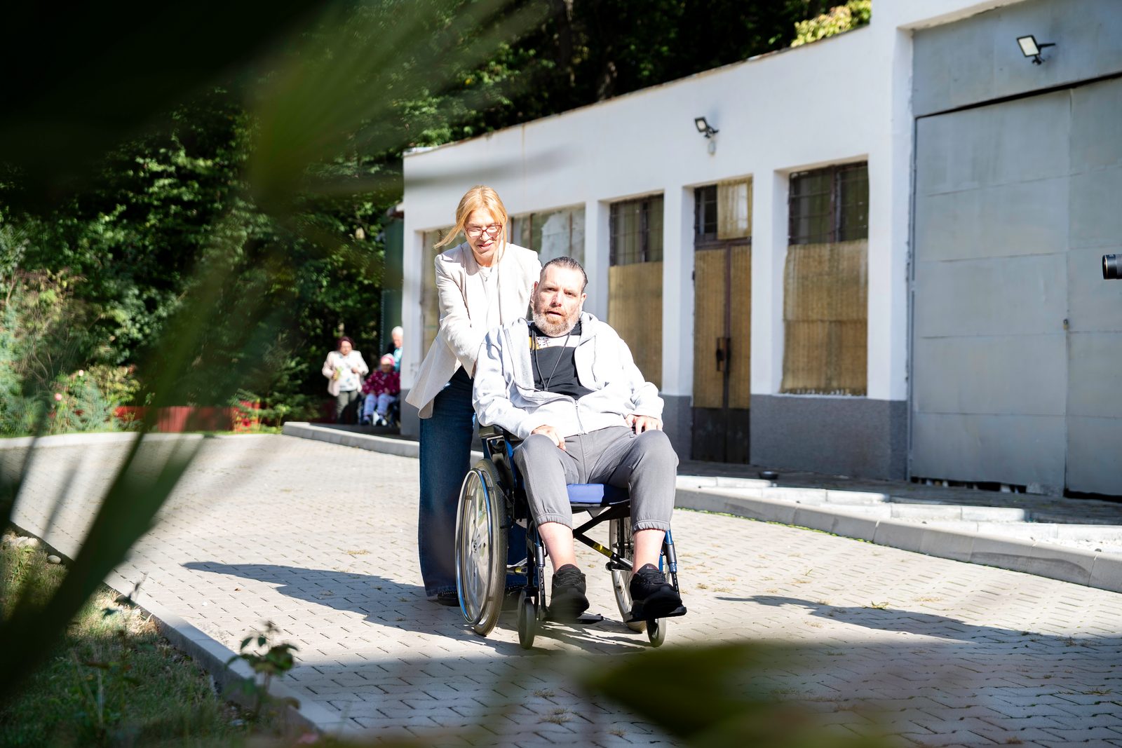 Pacient în scaun rulant, însoțit de asistentă în curtea spitalului
